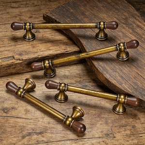 Könnte beinhalten: Fünf antike Schrankgriffe mit Bronze-Finish und dunkelbraunen Holzgriffen. Die Griffe sind auf einer rustikalen Holzoberfläche angeordnet und zeigen ihr Vintage-Design und ihre Hardware-Ästhetik.