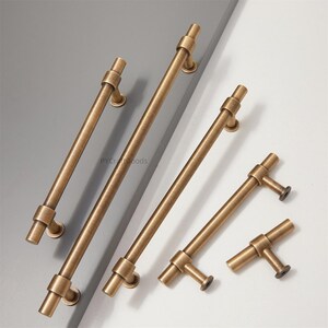 K&ouml;nnte beinhalten: Eine Auswahl an antiken Messing-Schrankgriffen und -Ziehgriffen. Die Hardware verf&uuml;gt &uuml;ber eine zylindrische Stange mit dekorativen Details und Montageplatten. Die Griffe sind in verschiedenen Gr&ouml;&szlig;en erh&auml;ltlich, mit einem warmen, gealterten Finish, geeignet f&uuml;r M&ouml;belrestaurierung oder Neubauten.