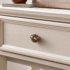 May include: Close-up of a light-coloured wooden drawer with a decorative, antique-style brass knob. The drawer is part of a larger piece of furniture, possibly a bedside table or dresser, with visible wood grain.