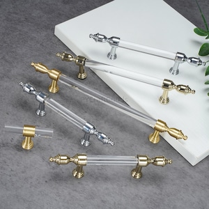Puede incluir: Un conjunto de tiradores para armarios con varillas de acrílico transparente y detalles metálicos. Los tiradores presentan acabados dorados y plateados, con remates decorativos. Ideal para muebles y decoración del hogar.