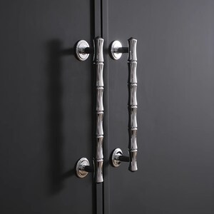 May include: Two polished chrome door handles with a bamboo stalk design. Each handle is mounted on a circular base and attached to a dark grey door. The handles are vertically aligned, adding a touch of nature-inspired elegance.
