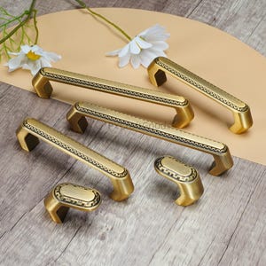May include: A collection of antique brass cabinet pulls and handles. The hardware features a rectangular design with a decorative border and curved ends. The pulls are in various sizes and shapes, suitable for drawers and cabinets.