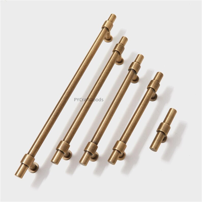 K&ouml;nnte beinhalten: Eine Sammlung von antiken Messing-Schrankgriffen in verschiedenen L&auml;ngen. Jeder Griff hat eine zylindrische Stange mit dekorativen Ringakzenten und kreisf&ouml;rmigen Montageplatten. Der Text "PYCraftGoods" ist sichtbar.