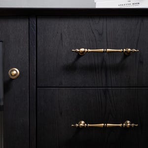 Peut inclure: Gros plan sur une armoire en bois noir avec deux tiroirs et une porte. L'armoire est orn&eacute;e de quincaillerie en laiton antique, notamment deux poign&eacute;es de tiroir et un bouton de porte rond. Le grain du bois est visible, ajoutant de la texture &agrave; la surface sombre.