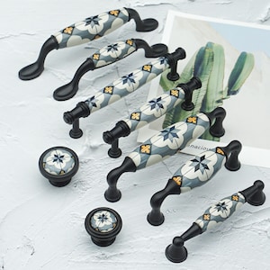 Pode incluir: Conjunto de ferragens decorativas para armários com puxadores e puxadores pretos com design cerâmico. A cerâmica apresenta um padrão de estrela azul, branco e amarelo. Os puxadores têm um design curvo e os puxadores são redondos.