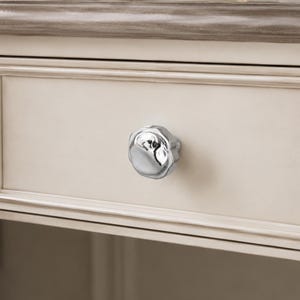 May include: A close-up of a cream-coloured drawer featuring a silver, flower-shaped knob. The drawer is part of a larger piece of furniture, with a decorative trim in a darker, muted colour.