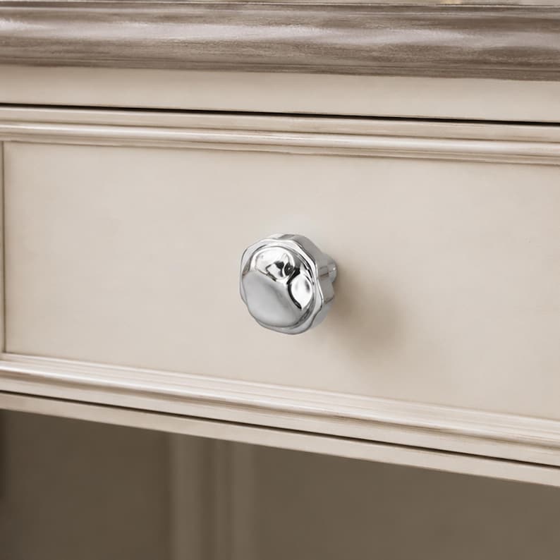 May include: A close-up of a cream-coloured drawer featuring a silver, flower-shaped knob. The drawer is part of a larger piece of furniture, with a decorative trim in a darker, muted colour.