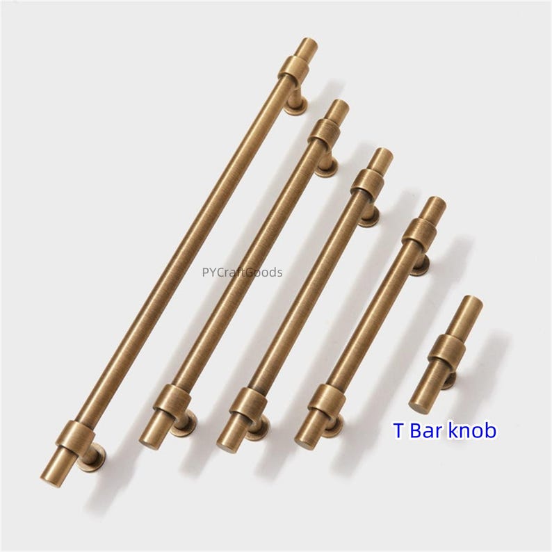 K&ouml;nnte beinhalten: Eine Auswahl an antiken Messing-T-Stangen-Schrankgriffen in verschiedenen L&auml;ngen. Die Hardware hat eine zylindrische Stange mit einem dekorativen Ring an jedem Ende. Der Text "T Bar knob" ist im Bild zu sehen.