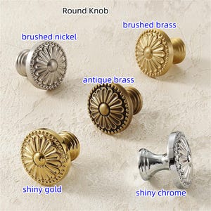 K&ouml;nnte beinhalten: Eine Auswahl an runden Kn&ouml;pfen in verschiedenen Ausf&uuml;hrungen: geb&uuml;rstetes Nickel, geb&uuml;rstetes Messing, antikes Messing, gl&auml;nzendes Gold und gl&auml;nzendes Chrom. Jeder Knopf hat ein florales Design und ist mit seiner Ausf&uuml;hrung beschriftet.
