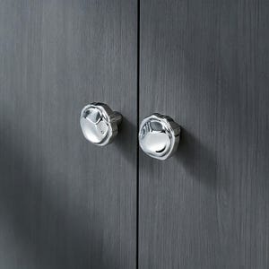 May include: Two polished silver cabinet knobs with a distinctive, textured pattern. They are fixed to a dark grey wooden cabinet door, offering a contemporary and stylish appearance. The knobs have a reflective surface.