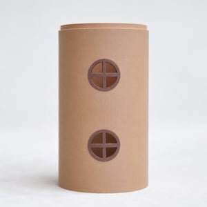 Puede incluir: Un objeto cilíndrico de color beige con un acabado mate liso, que presenta dos ventanas circulares apiladas verticalmente. Cada ventana tiene un marco marrón oscuro con un diseño de cruz, creando una apariencia simple y estructurada.