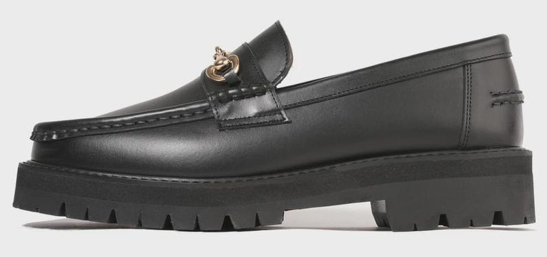 Peut inclure: Un mocassin en cuir noir dot&eacute; d'une &eacute;paisse semelle en caoutchouc crant&eacute;e et d'une cha&icirc;ne en m&eacute;tal dor&eacute; sur la bride sup&eacute;rieure. La chaussure pr&eacute;sente un bout arrondi, des coutures apparentes sur l'empeigne et un contrefort structur&eacute;.