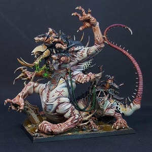 May include: A painted miniature figure of a multi-limbed, mutated creature with pale skin, red stitched markings, and a long, spiked tail. The creature features multiple heads, sharp claws, and green glowing vials connected by tubes to its body.