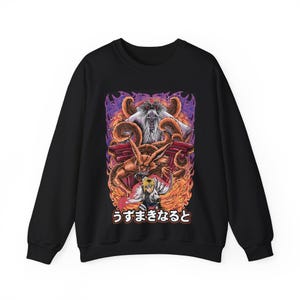 May include: Black sweatshirt featuring a vibrant graphic of a character with spiky blonde hair, a fiery fox, and a white-haired figure. The design includes Japanese text and a background of orange and purple flames.