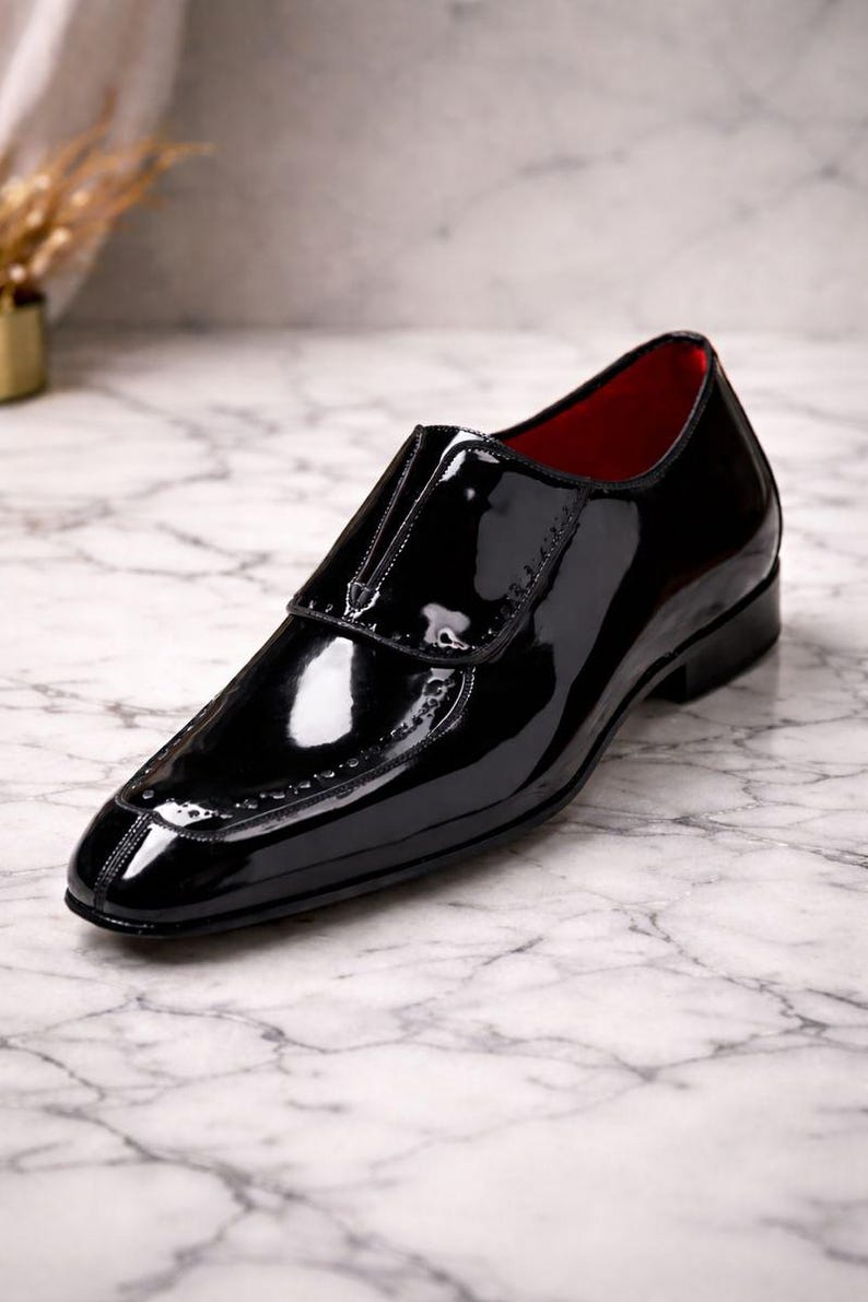 May include: A glossy black leather shoe with a red interior. The shoe features a sleek design with a pointed toe and decorative stitching along the edges. The shoe is a formal style.