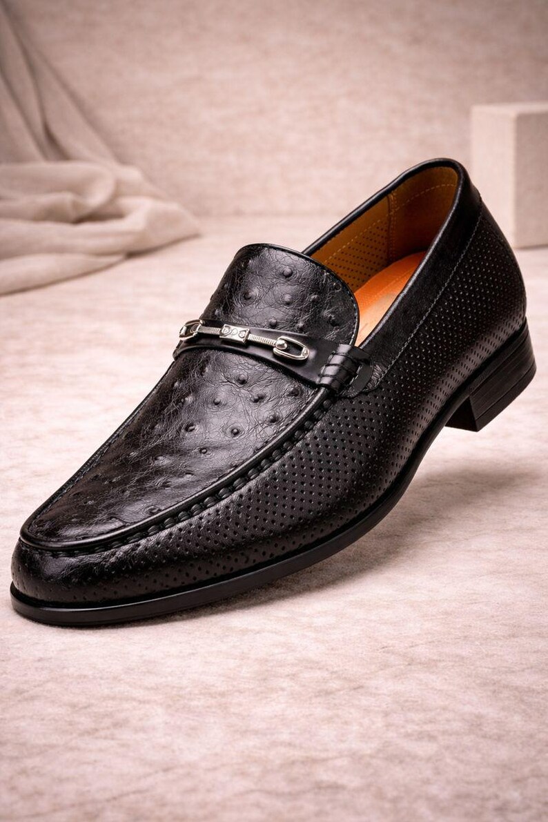 Pu&ograve; includere: Mocassino in pelle nera con un design strutturato e traforato. La scarpa presenta una fibbia color argento e un tacco basso. Lo stile &egrave; classico ed elegante, adatto a occasioni formali o semi-formali.