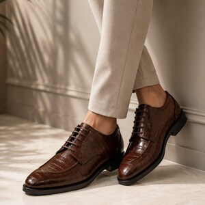 May include: A pair of dark brown leather oxford shoes featuring a glossy crocodile skin texture, a rounded toe, and matching dark brown laces. The shoes have a low black heel and a structured silhouette, providing a polished look for formal attire.