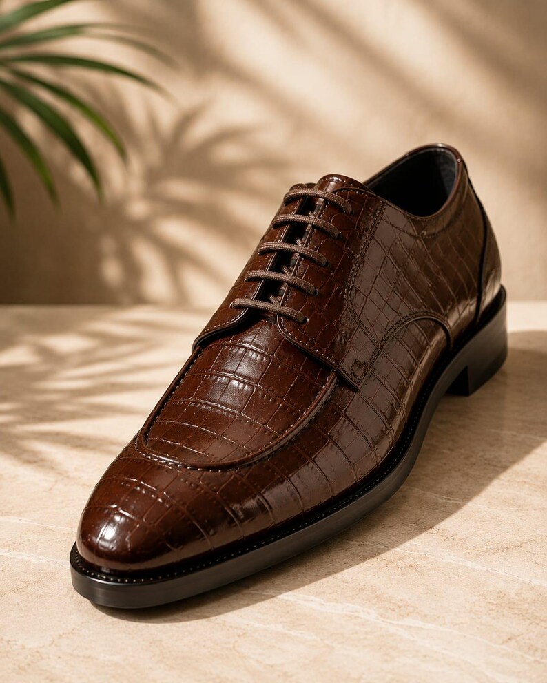 May include: A dark brown lace-up shoe with a glossy finish and a textured crocodile-skin pattern. The shoe features a rounded toe, a structured apron front, matching brown laces, and a solid black sole with a low heel for a classic silhouette.