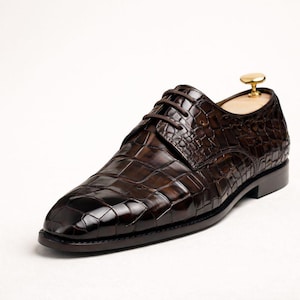May include: A brown leather dress shoe with a textured, crocodile-like pattern. The shoe has a classic lace-up design and a polished finish. The shoe is a size 10.