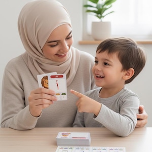 May include: A woman and a young child are looking at flashcards. The cards feature Arabic letters and illustrations, including a lion. A stack of similar cards and a learning mat with matching images are on the table.