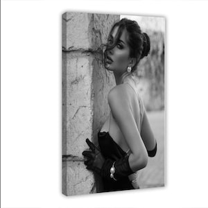 May include: Black and white canvas print of a woman in a black dress, leaning against a stone wall. She wears pearl earrings, a bracelet, and black gloves. The image is a portrait with a vintage aesthetic.