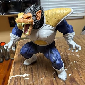 May include: A detailed figurine of a character from Dragon Ball Z. The figure is in a dynamic pose, with a fierce expression and open mouth. It features a white, blue, and yellow color scheme, with intricate details on the armor and face.
