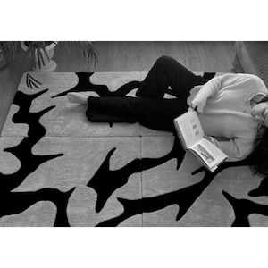 May include: A large rectangular area rug featuring a high-contrast black and white abstract pattern. The design consists of bold, irregular black shapes set against a light-colored background, creating a striking visual effect across the surface.