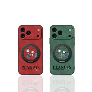 Puede incluir: Dos fundas para teléfono, una roja y otra verde, con un diseño de Peanuts. Cada funda tiene un soporte circular con Snoopy y Charlie Brown. El texto "PEANUTS CELEBRATING 70 YEARS" está impreso debajo.