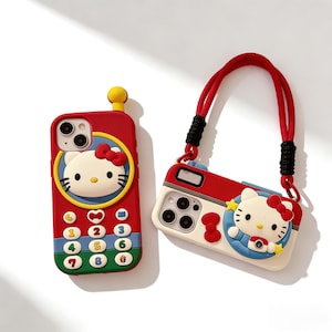 May include: Two phone cases featuring the character Hello Kitty. One is red and shaped like a phone with a keypad, the other is a camera-shaped case with a red strap. Both cases have a white Hello Kitty design with a red bow.
