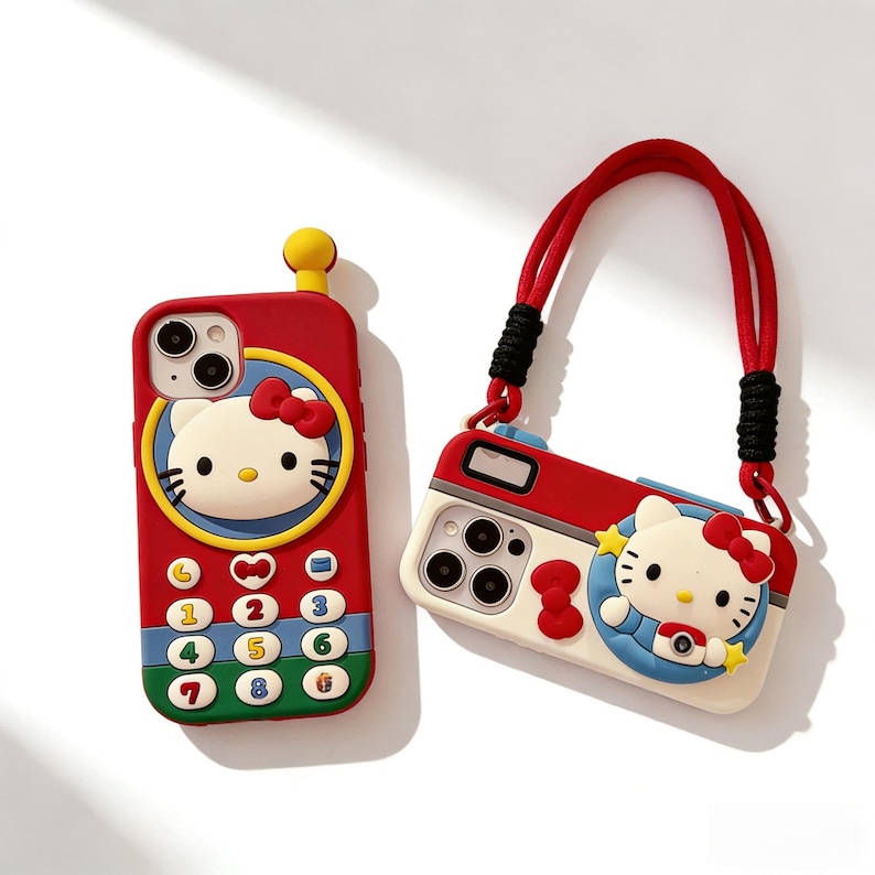 May include: Two phone cases featuring the character Hello Kitty. One is red and shaped like a phone with a keypad, the other is a camera-shaped case with a red strap. Both cases have a white Hello Kitty design with a red bow.