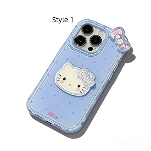 May include: A light blue phone case with a Hello Kitty design. The case has a clear border and features a 3D Hello Kitty face and bow, along with pink polka dots. The word "Nice" is printed on the bottom.