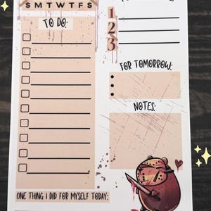 May include: A white notepad with a daily planner layout. The notepad features sections for "Today's Plan," "To Do," "Top Priorities," and "Notes." A cartoon bear with a knife is illustrated at the bottom. The notepad has a pink and brown color scheme.