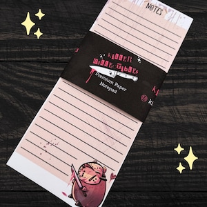 May include: A notepad with lined pages and a black band featuring the text "Killer Collectibles" and a knife illustration. The notepad has a cartoon illustration of a character holding a knife. The word "NOTES" is at the top.