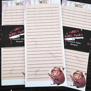 May include: Three lined notepads with the word "NOTES" at the top. Each notepad has a black band with the text "Killer Collectibles" and a knife graphic. A cartoon bear with a knife is at the bottom.