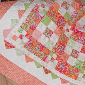 May include: A quilt with a patchwork design featuring floral patterns in shades of pink, green, and white. The quilt is made with a variety of fabrics and has a white background with a scalloped border.