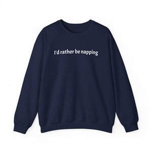 May include: A navy blue long-sleeve sweatshirt featuring the white text "I'd rather be napping" printed across the chest. The garment has a crew neckline, ribbed cuffs, and a ribbed hem, providing a standard fit with a solid dark blue colour.