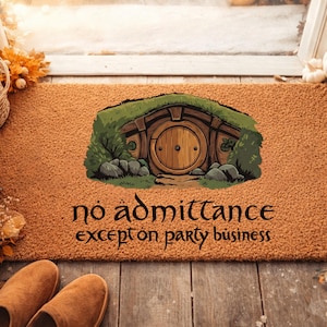 Op de afbeelding: Een rechthoekige deurmat met een bruine achtergrond en een afbeelding van een hobbitgat. Het hobbitgat heeft een houten deur en is omgeven door groen gras en rotsen. De tekst "no admittance except on party business" is in het zwart geschreven.