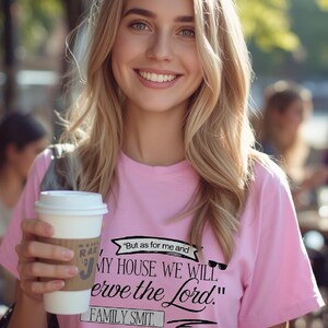 Puede incluir: Una camiseta rosa con el texto "But as for me and MY HOUSE, WE WILL serve the Lord. FAMILY SMIT." Una mujer lleva la camiseta y sostiene una taza de café con una funda marrón.
