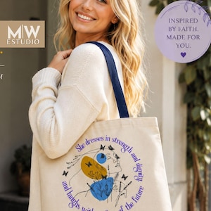 Puede incluir: Un bolso de tela color crema con asas azul oscuro, que presenta un gráfico del perfil de una mujer, mariposas y elementos florales. El texto dice: She dresses in strength and dignity, and laughs without fear of the future. Margot.