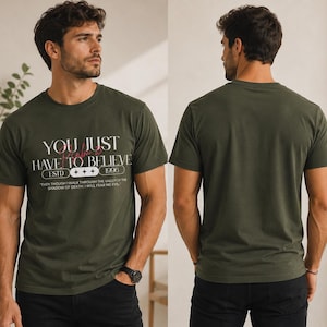 Puede incluir: Camiseta verde oliva con el texto "YOU JUST HAVE TO BELIEVE" en blanco y rosa. La camiseta también presenta el texto "ESTD 1996" y una cita. El modelo lleva un reloj negro y pantalones negros. La parte trasera de la camiseta es verde oliva liso.