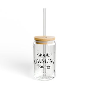 Puede incluir: Un vaso de vidrio transparente con tapa de bambú y pajita transparente. El vaso tiene la inscripción "Sippin' GEMINI Energy" en negro. Pequeñas estrellas están impresas en el vidrio.