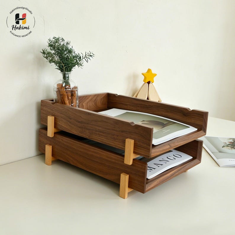 K&ouml;nnte beinhalten: Ein zweistufiger Schreibtisch-Organizer aus Holz mit dunkelbraunem Finish. Der Organizer hat eine rechteckige Form mit hellbraunen St&uuml;tzen. Das obere Fach enth&auml;lt eine Zeitschrift, und das untere Fach tr&auml;gt das Wort "MANGO".