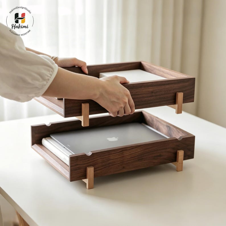 K&ouml;nnte beinhalten: Zweistufiger Schreibtisch-Organizer aus Holz mit dunkelbraunem Finish. Der Organizer hat eine rechteckige Form mit hellfarbigen Holzbeinen. Ein Laptop befindet sich im unteren Fach. Eine Person hebt das obere Fach an.