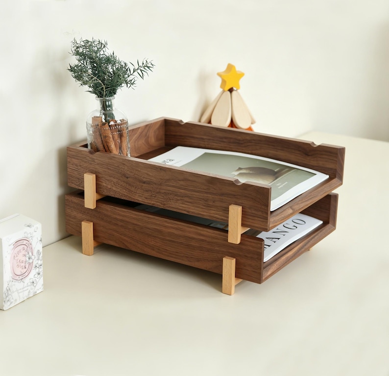 K&ouml;nnte beinhalten: Ein zweistufiger Schreibtisch-Organizer aus Holz mit dunkelbraunem Finish. Der Organizer hat eine rechteckige Form mit einem Tablett oben und einem zweiten Tablett darunter. Die Tabletts werden von hellfarbigen Holzst&uuml;tzen getragen. Oben steht eine kleine Glasvase mit Gr&uuml;nzeug.