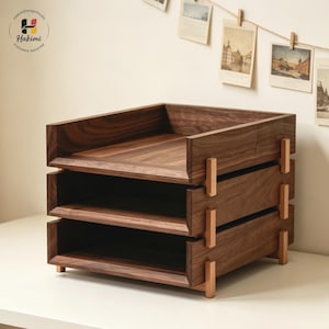 K&ouml;nnte beinhalten: Ein dreistufiger Schreibtisch-Organizer aus Holz mit dunkler, brauner Oberfl&auml;che. Der Organizer hat eine rechteckige Form mit offenen F&auml;chern und wird von kleinen Holzbeinen getragen. Das Design weist eine Kombination aus horizontalen und vertikalen Holzelementen auf.