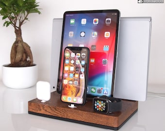 May include: A wooden charging station with a dark finish holds an iPad, iPhone, Apple Watch, and a white charging accessory. A small bonsai tree in a white pot is to the left. The charging station has a black base and the brand name "valliswood" is in the top right corner.