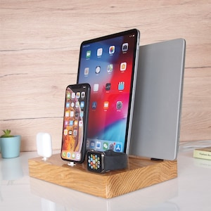 May include: A wooden charging station with a gray laptop, a tablet, a smartphone, and a smartwatch. The station has a white charging pad for a wireless charger.