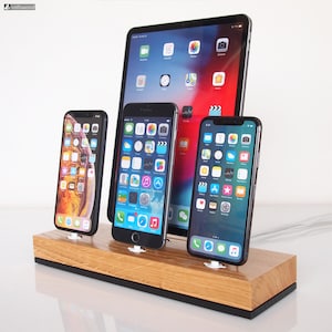 Op de afbeelding: Een houten oplaadstation met een tablet en drie smartphones. De apparaten staan voor de tablet en tonen app-pictogrammen op hun schermen. Het station is gemaakt van lichtgekleurd hout met een donkere basis.