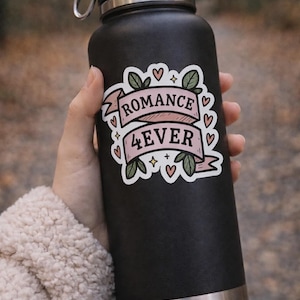 May include: Black water bottle with a silver rim and handle. A sticker on the bottle reads "ROMANCE 4EVER" in pink lettering, with green leaves, hearts, and stars. The bottle is held by a person.