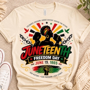 以下が含まれることがあります： クリーム色のTシャツ。Juneteenthを祝うグラフィックが特徴です。デザインはシルエット、鎖、そして「Juneteenth Freedom Day June 19, 1865」の文字が描かれています。また、「Celebrate Freedom, Honor History, Inspire the Future」と「Our History. Our Freedom. Our Legacy.」のフレーズも含まれています。